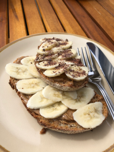 two slices of toast with peanut butter, covered in thin slices of banana. Top slice has grated dark chocolate.